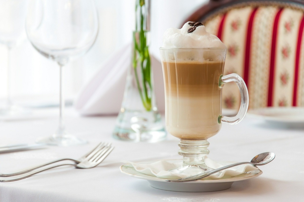 Кофейный напиток латте в высоком стеклянном бокале стоит на сервированном столе в кафе