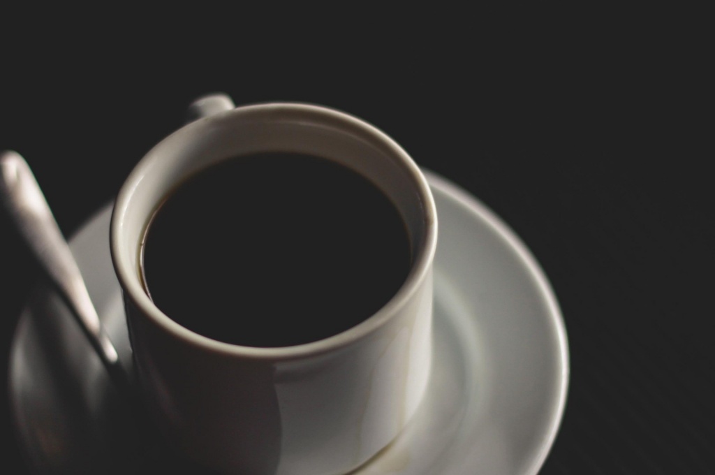 Белая чашка чёрного кофе на блюдце с ложкой