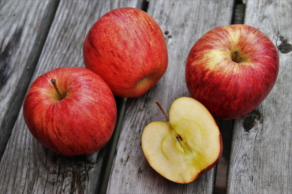 Три целых красных яблока и одна половина яблока лежат на деревянном столе